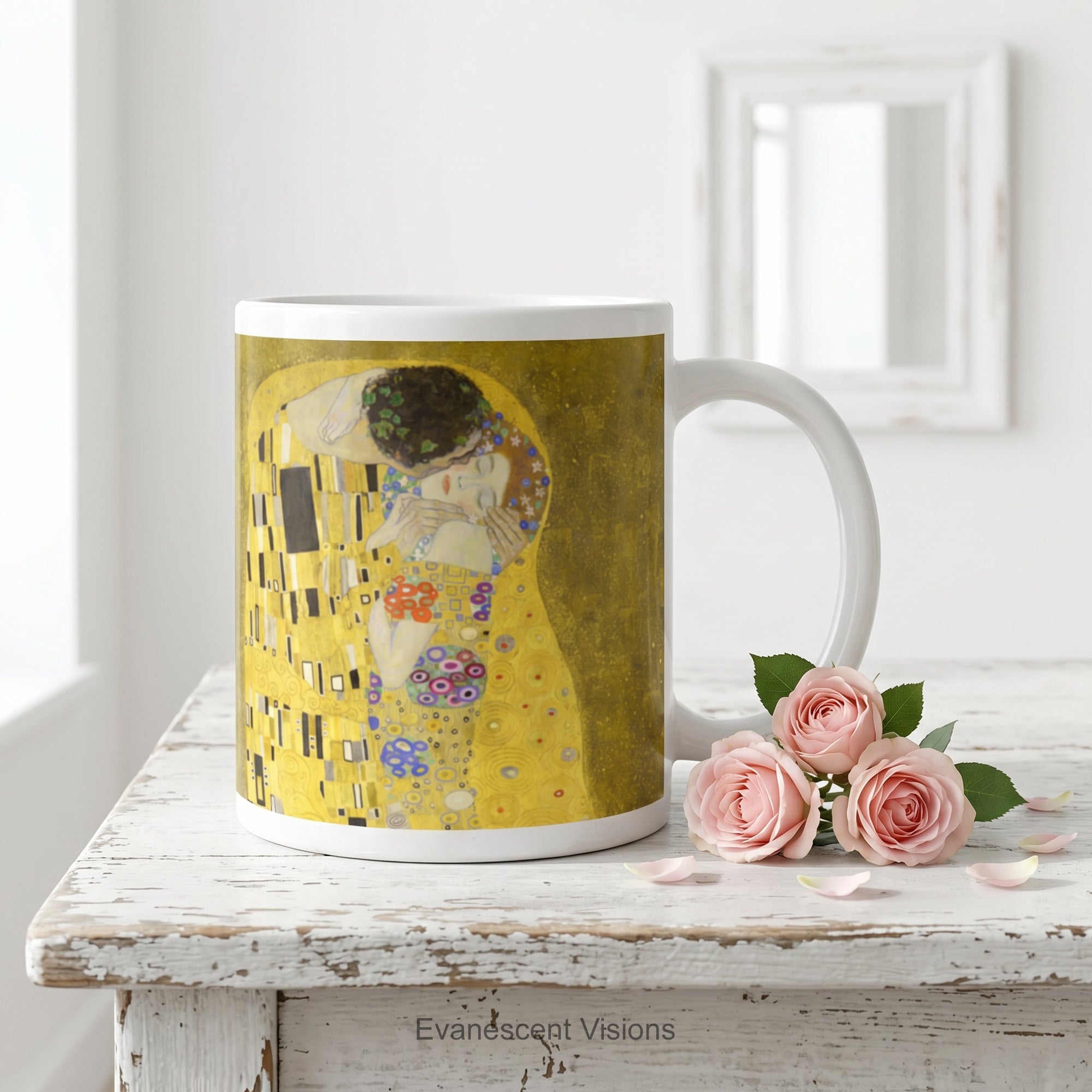 A white ceramic mug featuring a print of  Gustav Klimt's 'The Kiss' painting shown on a white wood table with small pink roses. 