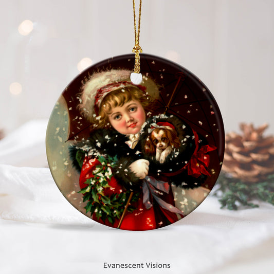 Ceramic Christmas Ornament with design of little girl holding a puppy in a muff in the snow. In the background a fir cone.