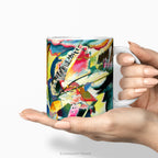 Hands holding aceramic mug featuring abstract painting 'Improvisation Klamm' by Kandinsky.
