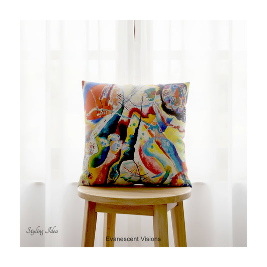 A square cushion featuring a print of the  abstract, multicolored painting 'Bild mit Rotem Fleck' by Wassily Kandinsky, shown on a stool against a sheer white curtained window. 