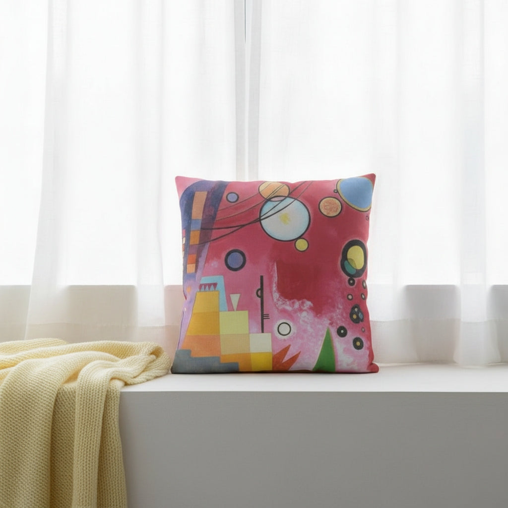 A colourful square cushion featuring an abstract art print of Schweres Rot (Heavy Red) by abstract artist Wassily Kandinsky, styled on a white window seat. 