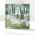 A square art greeting card on a table  featuring Gustav Klimt impressionistic painting 'Church at Cassone' a village scene with white buildings, green trees, and blue-gray sky.