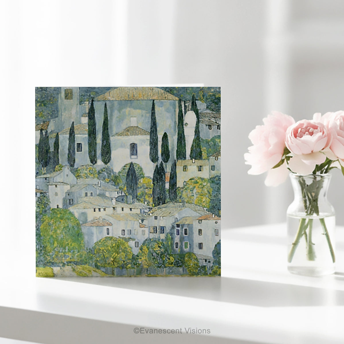 A square art greeting card on a table w featuring Gustav Klimt impressionistic painting 'Church at Cassone' a village scene with white buildings, green trees, and blue-gray sky.