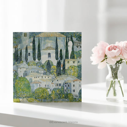 A square art greeting card on a table w featuring Gustav Klimt impressionistic painting 'Church at Cassone' a village scene with white buildings, green trees, and blue-gray sky.
