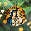 Ceramic Christmas ornament with stained glass window detail of Mary and Jesus. The ornament hangs with a gold thread from a Christmas tree and is surrounded by golden hearts and circles.