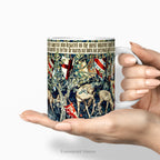 Hands holding a ceramic mug with a print of tapestry design 'Verdure with Shields and Deer'.