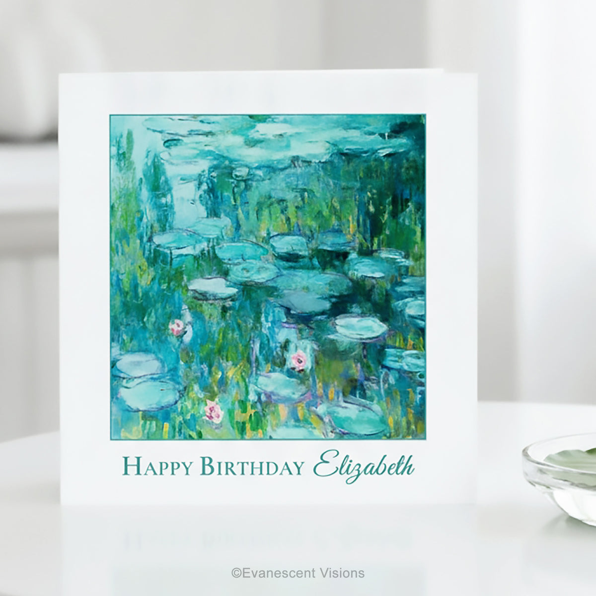 A white greeting card standing on a white surface, featuring Claude Monet's impressionist Water Lilies Painting in blue, green, and teal tones with the text 'Happy Birthday Elizabeth' below the artwork. 