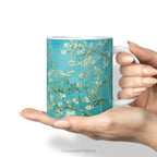 A hand holding the ceramic mug featuring Vincent van Gogh's 'Almond Blossom' painting design.