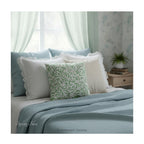A square decorative cushion with green botanical pattern titled 'Willow Bough' by William Morris, shown styled on a bed with white and blue linens.