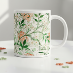 A white ceramic mug featuring a botanical pattern of white and orange flowers, green leaves,  titled 'Jasmin by William Morris, shown on a white table.