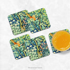 Set of four coasters printed with detail from the design  'Cock Pheasant' by William Morris, shown on a marble counter with a glass of orange