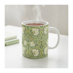 A ceramic mug styled on a table with floral patterned artwork titled 'Pimpernel' by William Morris. 