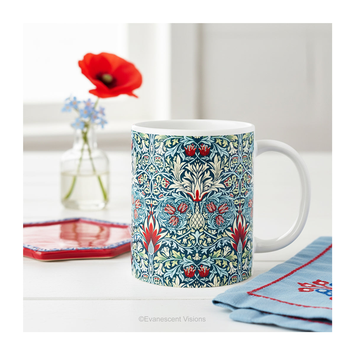 A  ceramic mug featuring a print of floral pattern 'Snakeshead' by William Morris, on a table.