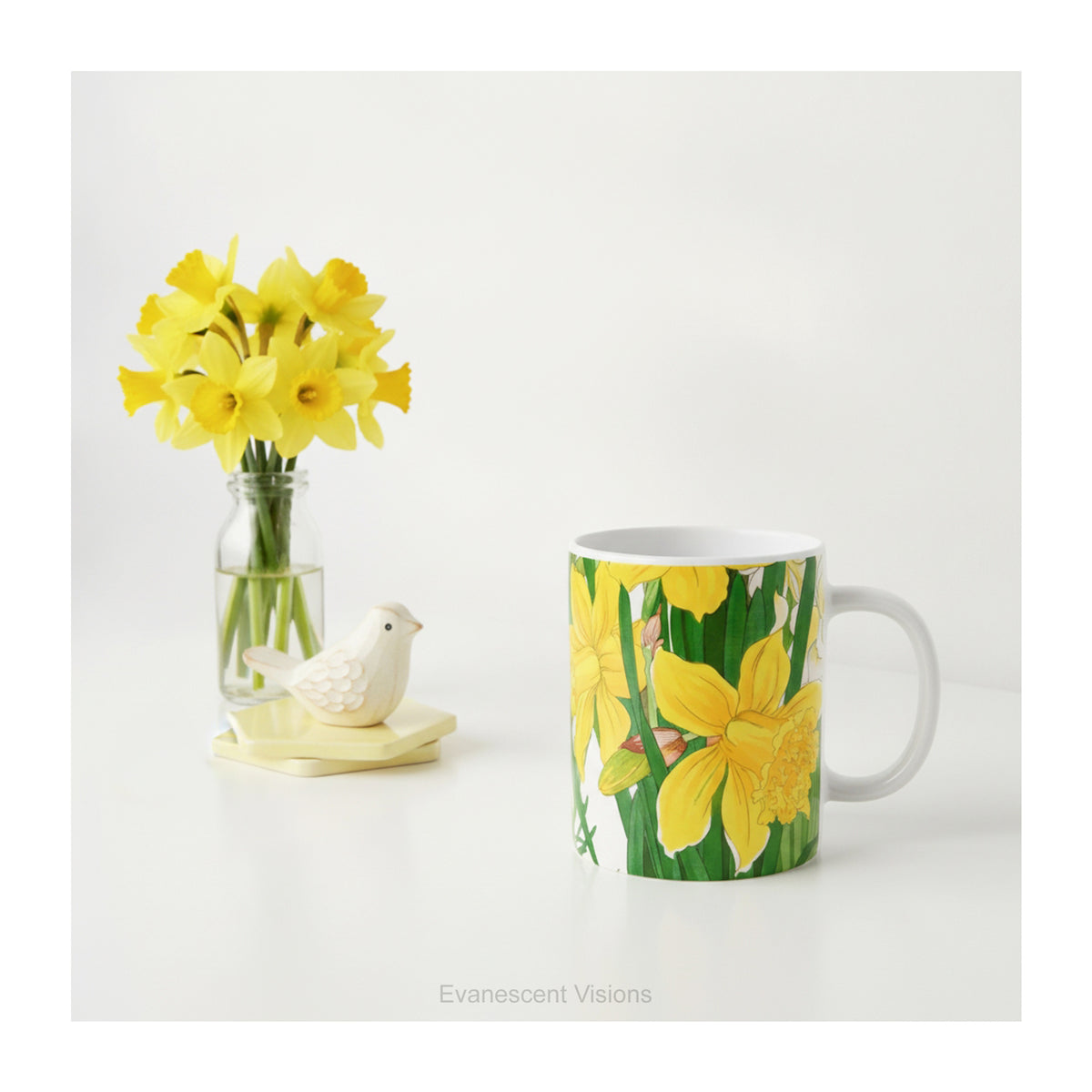 A ceramic mug with a print of painting of 'Spring Daffodil Flowers' styled on a table with a vase of daffodils