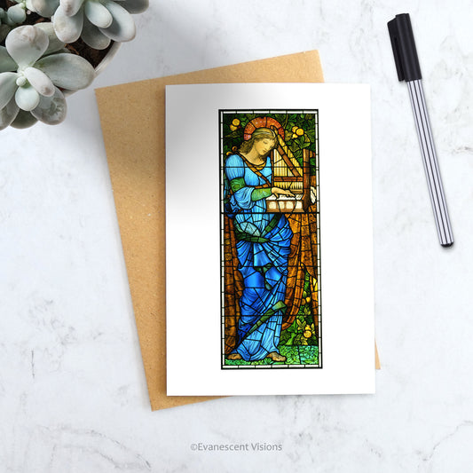 Burne-Jones Saint Cecilia Religious Greeting Card on a table with a pen and plant