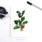 Holly Christmas Greeting Card on a desk with pens